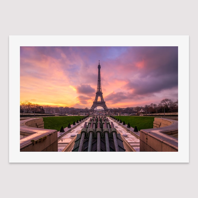 Puede incluir: Impresi&oacute;n enmarcada de la Torre Eiffel en Par&iacute;s al atardecer. El cielo es una mezcla de tonos naranja, rosa y morado. La torre se recorta contra el cielo colorido, con una fuente y c&eacute;sped verde en primer plano.