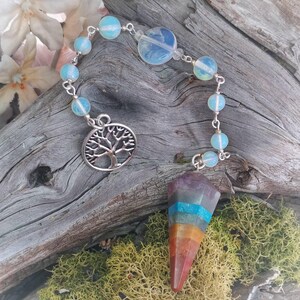 Puede incluir: Un p&eacute;ndulo de chakra arco&iacute;ris con un dije de &aacute;rbol de la vida plateado y una cadena de cuentas iridiscentes.