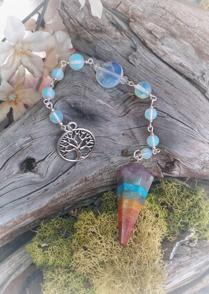 Puede incluir: Un p&eacute;ndulo de chakra arco&iacute;ris con un dije de &aacute;rbol de la vida plateado y una cadena de cuentas iridiscentes.