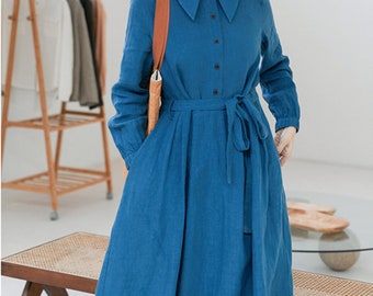 May include: A long-sleeved, blue linen dress with a large collar, button closure, and a tie belt. The dress has a relaxed fit and a slightly flared skirt.