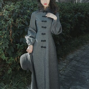 May include: A gray long-sleeved dress with a high collar and black bow details. The dress has a fitted bodice and a flowing skirt.