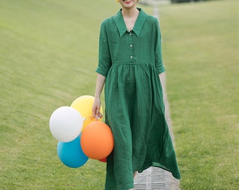 May include: A woman wearing a green linen dress with a collared neckline and button-down front. She is holding a bunch of colorful balloons: white, yellow, blue, and orange. The dress has a relaxed fit and three-quarter sleeves.