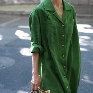 May include: A long-sleeved, green linen shirt dress with a collared neckline and button closure. The dress has a relaxed fit and features a chest pocket.