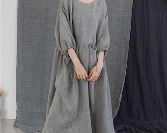 May include: A gray linen dress with a round neckline and 3/4 sleeves. The dress has a gathered waist and a relaxed fit.