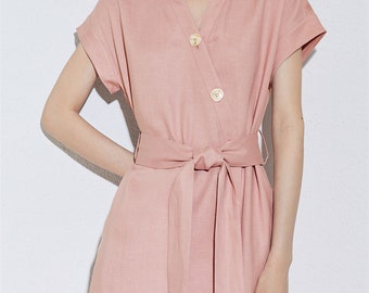 May include: A blush pink linen dress with a V-neckline, short sleeves, and a self-tie belt. The dress has a button closure at the front.