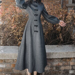 May include: A gray long-sleeved dress with a high collar and a row of black buttons down the front. The dress has a fitted bodice and a flared skirt.