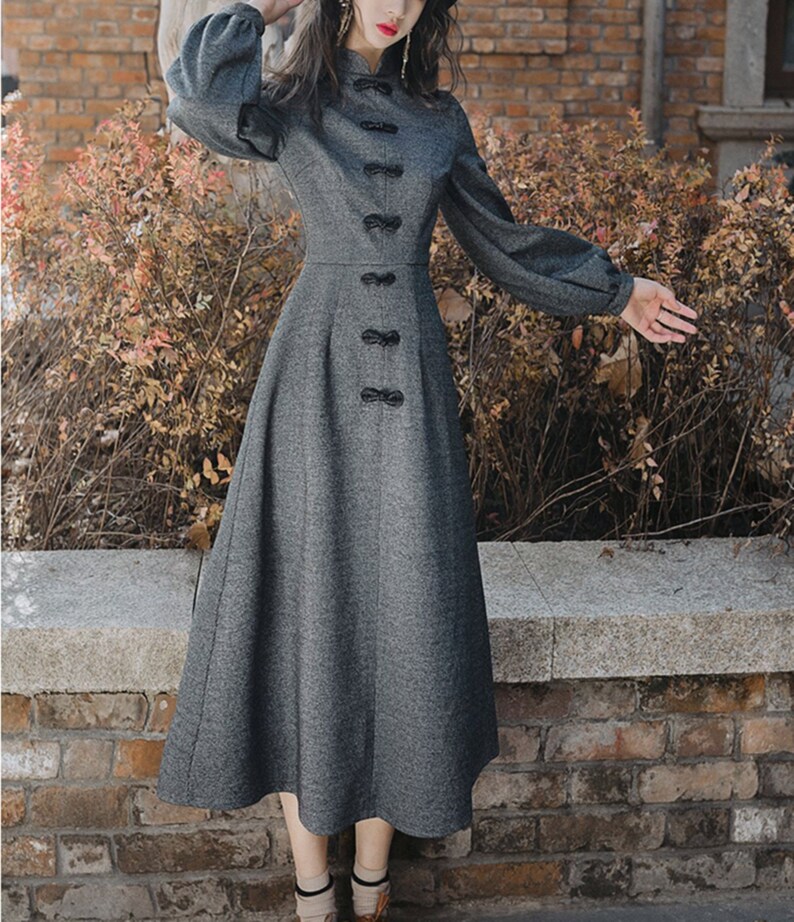 May include: A gray long-sleeved dress with a high collar and a row of black buttons down the front. The dress has a fitted bodice and a flared skirt.