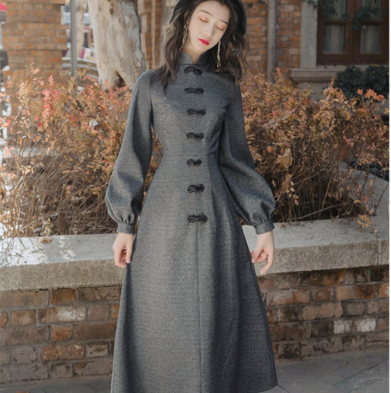 May include: A gray long-sleeved dress with a mandarin collar and a row of black buttons down the front. The dress has a fitted bodice and a flared skirt.
