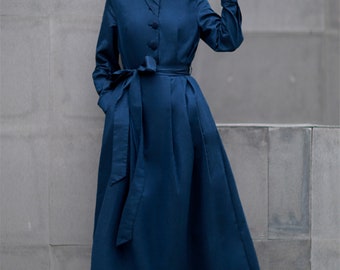 May include: A long-sleeved, dark blue dress with a high collar and a matching belt. The dress has a simple, elegant design and is made of a smooth, flowing fabric.