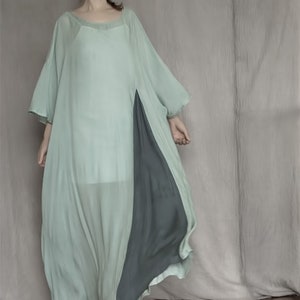 Può includere: Un abito maxi fluido di colore verde chiaro con un pannello lungo di colore verde scuro sul lato. L'abito ha una vestibilità ampia e comoda e una scollatura rotonda.