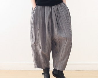 May include: Gray linen pants with a wide leg and a loose fit. The pants have a pleated waistband and large pockets on the sides.