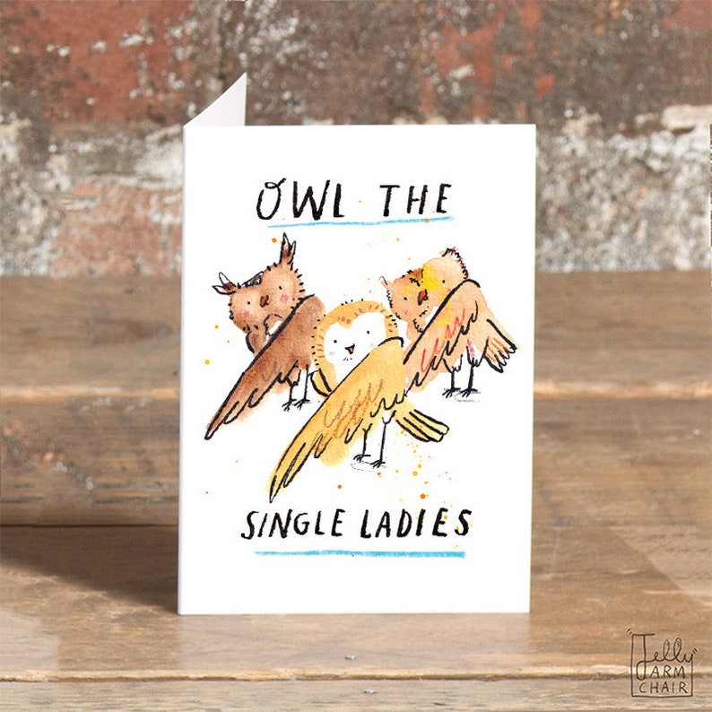 May include: A white card with a watercolor illustration of three owls. The owls are brown and yellow with black eyes. The text "Owl the single ladies" is written in black below the owls.