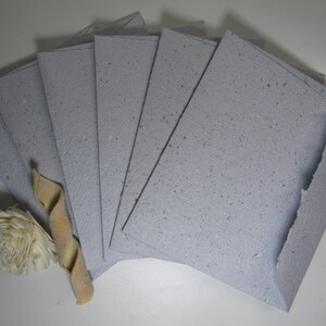 May include: A stack of eight light gray paper envelopes with a speckled texture. The envelopes are arranged in a fan shape.