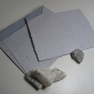 May include: Three sheets of light gray handmade paper with a speckled texture. The paper is folded in half and has a rough, uneven edge.