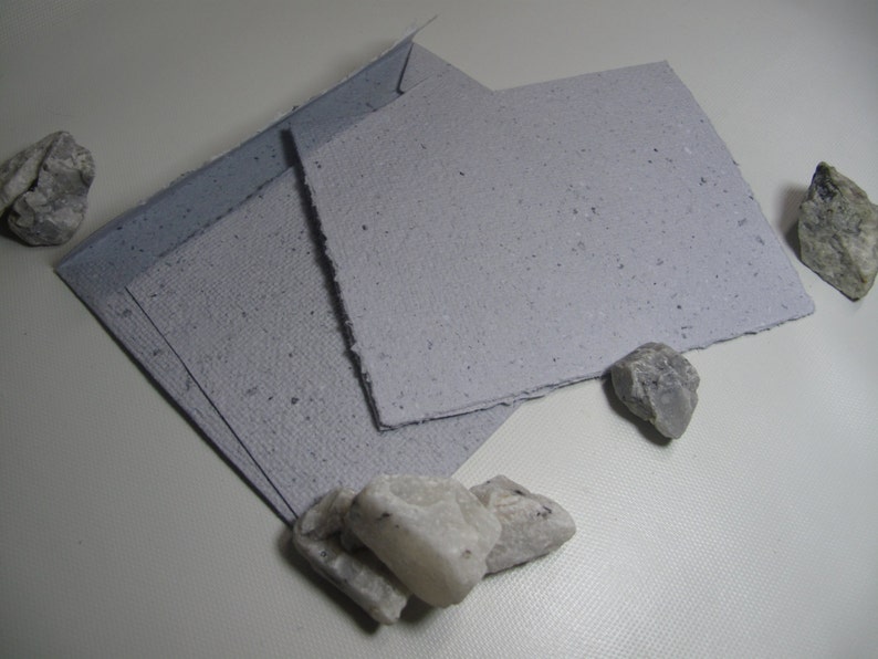 May include: Three sheets of light gray handmade paper with a speckled texture. The paper is folded in half and has a rough, uneven edge.