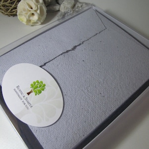 May include: A light purple envelope with a textured surface, packaged in a clear plastic box. The envelope has a white oval sticker with a green tree and the text "Rustic & Simple Handmade for You".
