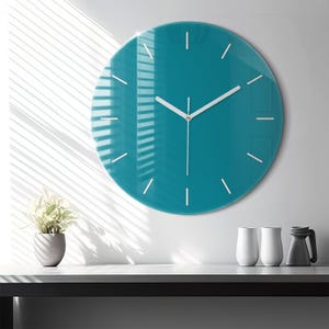 May include: A circular wall clock with a glossy teal face and white hour markers. The clock features thin white hour, minute, and second hands centered on the dial. The design is simple and clean, with no numbers, providing a clear view of the time.