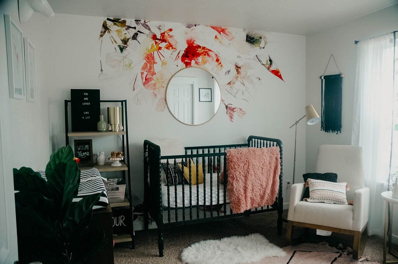 May include: A nursery room with a black crib, a white rocking chair, a black shelf with a sign that says "Welcome Home", and a floral wall decal.