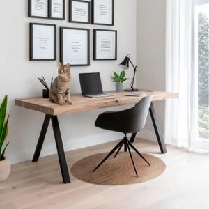 Könnte beinhalten: Ein heller Holzschreibtisch mit schwarzen Metallbeinen und einem schwarzen Bürostuhl. Eine Katze sitzt auf dem Schreibtisch neben einem Laptop. Eine kleine Topfpflanze und eine Lampe stehen ebenfalls auf dem Schreibtisch. Der Schreibtisch befindet sich in einem Raum mit weißen Wänden und einem Fenster mit weißen Vorhängen.