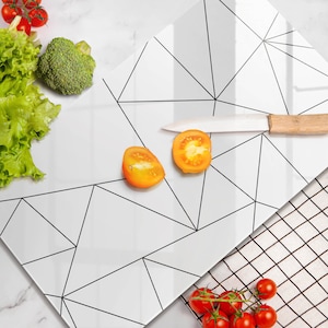 Puede incluir: Una tabla de cortar de vidrio blanco con un patrón geométrico negro. La tabla tiene dos tomates cortados por la mitad y un cuchillo encima. Hay tomates en una rejilla de alambre en el fondo.