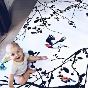 May include: A baby sits on a white and black wallpaper roll with a black silhouette of branches and colorful birds. The wallpaper has a repeating pattern of branches and birds.