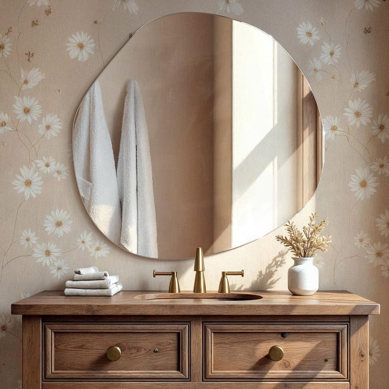 Peut inclure: Une vasque de salle de bain en bois avec deux tiroirs et un lavabo en porcelaine blanche. La vasque est dot&eacute;e de ferrures dor&eacute;es et d'un robinet dor&eacute;. Un miroir rond &agrave; cadre dor&eacute; est suspendu au-dessus du lavabo. L'arri&egrave;re-plan est un papier peint beige &agrave; motif floral blanc.