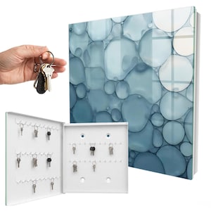 Peut inclure: Une armoire à clés murale dotée d'un panneau avant brillant avec un motif abstrait de bulles bleues et blanches. L'intérieur est blanc avec plusieurs crochets métalliques pour suspendre les clés, montrée fermée et ouverte avec des clés.