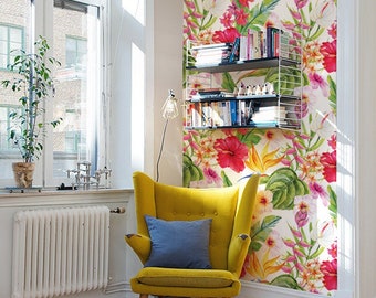 May include: A yellow armchair with a blue pillow sits in a corner of a room with a white wall covered in a tropical floral wallpaper. A white radiator is visible on the left side of the image. A bookshelf with books and decorative items is on the wall behind the chair.