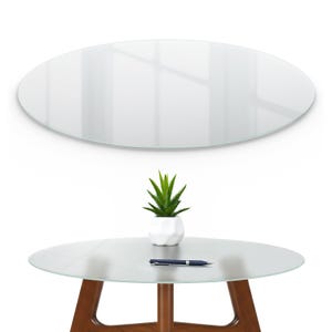 May include: A clear oval glass tabletop with a small succulent plant in a white geometric pot and a blue pen on a round table with wooden legs. A matching oval glass piece is above.