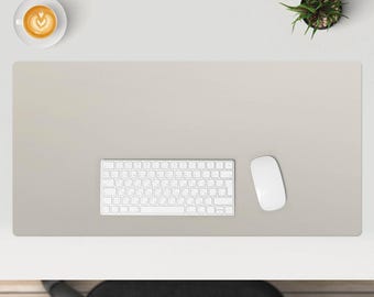May include: A white keyboard and mouse on a light gray desk mat. The desk mat is on a white desk with a cup of coffee and a potted plant in the background.
