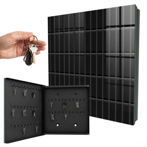 Può includere: Un armadietto portachiavi da parete nero con un pannello frontale lucido a piastrelle rettangolari. L'armadietto si apre rivelando un interno nero opaco con molteplici ganci metallici disposti in file, con diverse chiavi argentate appese.