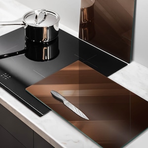 May include: A brown glass cutting board with a silver knife on top of it. The cutting board is sitting on a black electric stovetop.