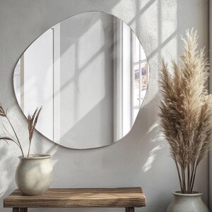 Peut inclure: Un grand miroir de forme organique avec une surface lisse et r&eacute;fl&eacute;chissante. Le miroir est accroch&eacute; &agrave; un mur blanc et refl&egrave;te une fen&ecirc;tre avec la lumi&egrave;re du soleil qui traverse.