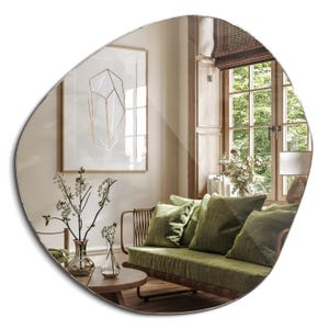 Peut inclure: Un grand miroir de forme irr&eacute;guli&egrave;re avec un bord biseaut&eacute;, refl&eacute;tant un salon avec un canap&eacute; vert, une table basse en bois et une estampe encadr&eacute;e d'un motif g&eacute;om&eacute;trique.