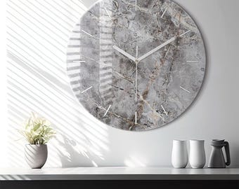 May include: A circular wall clock featuring a grey and white marble pattern on its face. The clock has thin white hour markers and two slender white hands. The surface has a glossy finish that reflects light, creating a smooth and polished appearance.