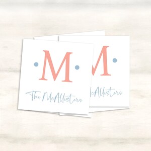 K&ouml;nnte beinhalten: Drei wei&szlig;e quadratische Karten mit dem Buchstaben "M" in Rosa und zwei blauen Punkten auf jeder Karte. Der Text "The McAllisters" ist in blauer Kursivschrift auf der Unterseite der linken Karte und "McAllisters" ist in blauer Kursivschrift auf der Unterseite der rechten Karte geschrieben.