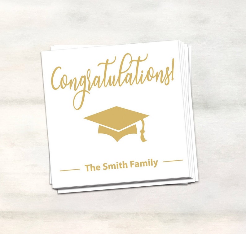 Puede incluir: Tarjeta blanca con texto dorado que dice "&iexcl;Felicidades!" y un icono de gorro de graduaci&oacute;n dorado. La tarjeta tambi&eacute;n tiene el texto "The Smith Family" en dorado.