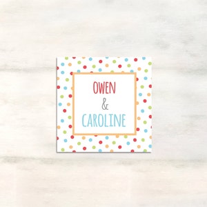 Puede incluir: Una tarjeta blanca con un patr&oacute;n de lunares de colores. La tarjeta tiene un borde rojo y el texto "Owen & Caroline" en el centro.