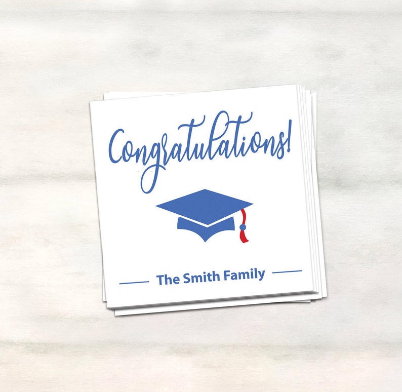Puede incluir: Tarjeta blanca con texto azul en cursiva que dice "&iexcl;Felicidades!" y un gorro de graduaci&oacute;n azul con una borla roja. La tarjeta tambi&eacute;n tiene una l&iacute;nea con el texto "The Smith Family" impreso debajo del gorro.