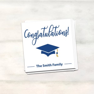 Puede incluir: Tarjeta blanca con texto azul y dorado que dice "&iexcl;Felicidades!" con un icono de gorro de graduaci&oacute;n azul y el texto "The Smith Family" en negro.