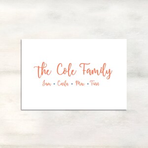 May include: A white card with the text "The Cole Family" in orange cursive lettering. Below the text are the names "Sam, Carla, Mac, Finn" in smaller orange lettering.