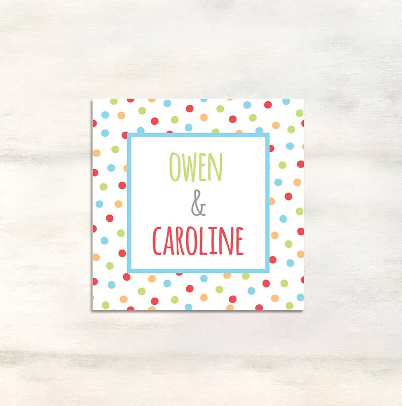 Puede incluir: Una tarjeta blanca con un borde azul y lunares de colores. El texto "Owen & Caroline" est&aacute; escrito en verde y rojo.