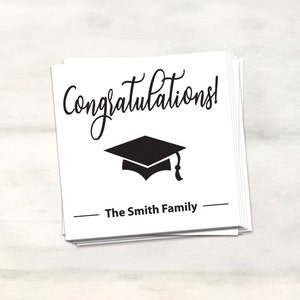 Puede incluir: Tarjeta blanca con texto negro que dice "&iexcl;Felicidades!" y un gorro de graduaci&oacute;n negro. La tarjeta tambi&eacute;n tiene el texto "The Smith Family" en negro.