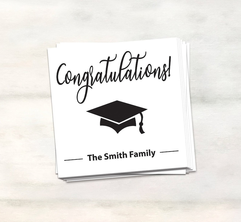 Puede incluir: Tarjeta blanca con texto negro que dice "&iexcl;Felicidades!" y un gorro de graduaci&oacute;n negro. La tarjeta tambi&eacute;n tiene el texto "The Smith Family" en negro.