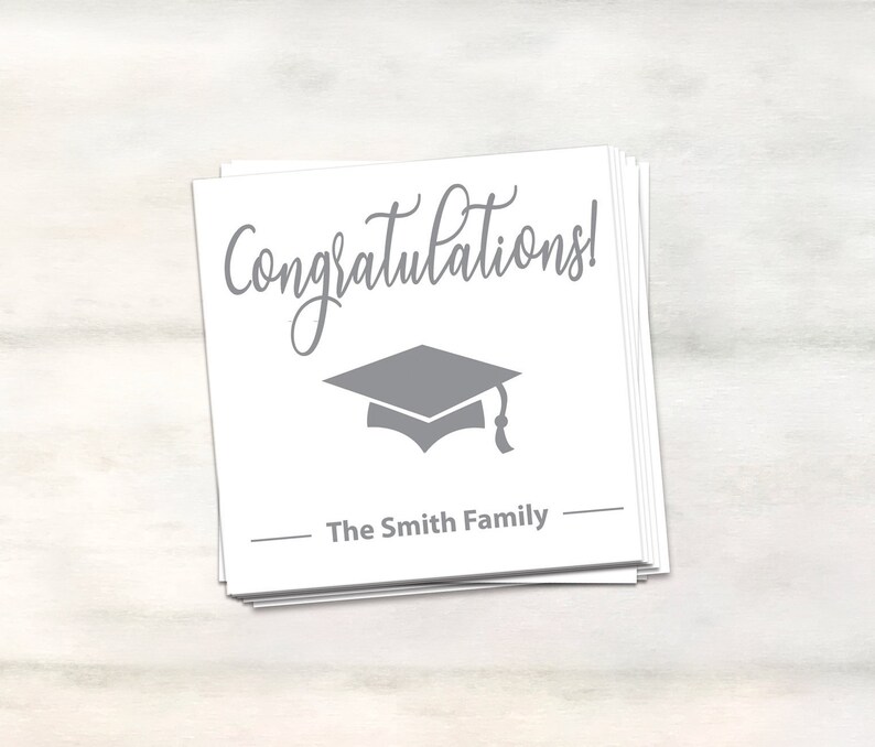 Puede incluir: Tarjeta blanca con texto gris que dice "&iexcl;Felicidades!" y un gorro de graduaci&oacute;n gris. La tarjeta tambi&eacute;n tiene el texto "The Smith Family" en gris.