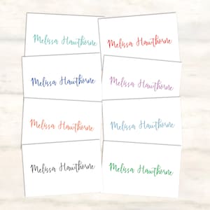 May include: Eight white cards with the name "Melissa Hawthorne" written in different colors of ink: teal, red, blue, purple, orange, light blue, dark blue, and green.