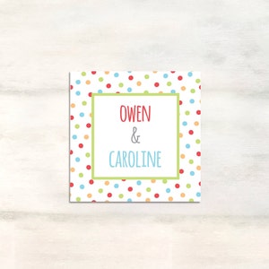 Puede incluir: Una tarjeta blanca con un patr&oacute;n de lunares de colores. La tarjeta tiene un borde verde alrededor de un rect&aacute;ngulo blanco con el texto "Owen & Caroline" en rojo y gris.