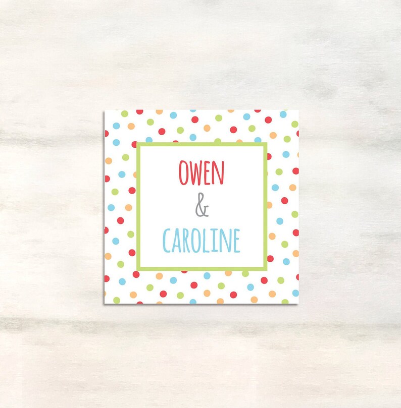 Puede incluir: Una tarjeta blanca con un patr&oacute;n de lunares de colores. La tarjeta tiene un borde verde alrededor de un rect&aacute;ngulo blanco con el texto "Owen & Caroline" en rojo y gris.