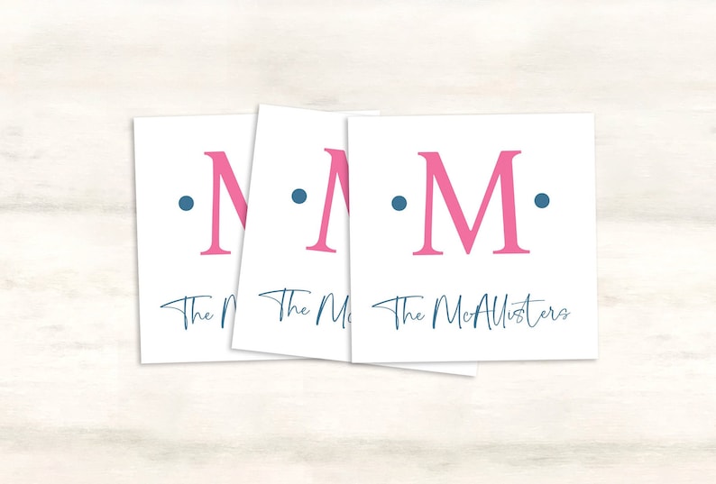 K&ouml;nnte beinhalten: Drei wei&szlig;e Karten mit einem rosa Buchstaben "M" und zwei blauen Punkten auf jeder Karte. Der Text "The McAllisters" ist in blauer Kursivschrift auf der untersten Karte rechts geschrieben.
