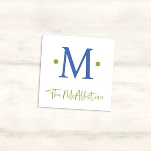 K&ouml;nnte beinhalten: Eine wei&szlig;e Karte mit einem blauen "M" umgeben von zwei gr&uuml;nen Punkten. Der Text "The McAllisters" ist in gr&uuml;ner Kursivschrift unter dem Buchstaben geschrieben.